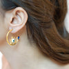Raya gold plated open hoop evil eye earrings with blue and white enamel worn by a model by Eda Jewels Dubai